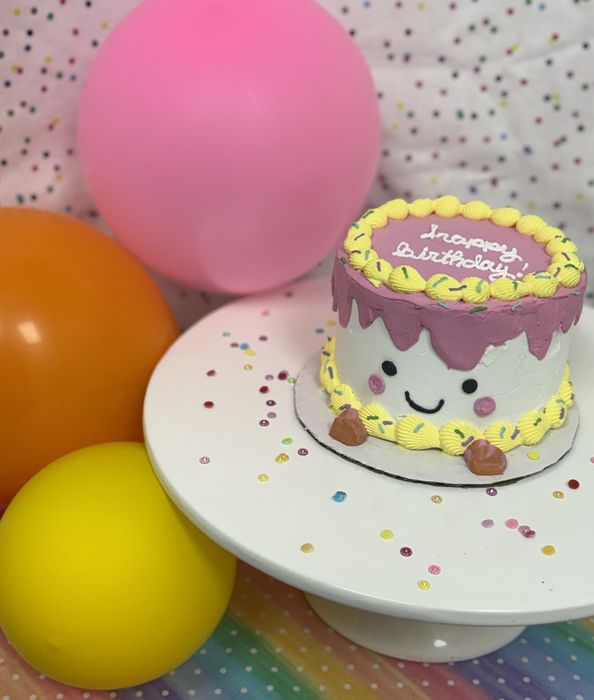 Small smiling birthday cake with purple drip and yellow piping