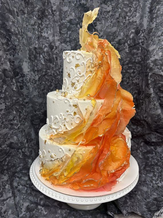 Three-tier white wedding cake with a cascading wave of orange, gold, and yellow wafer-paper ruffles