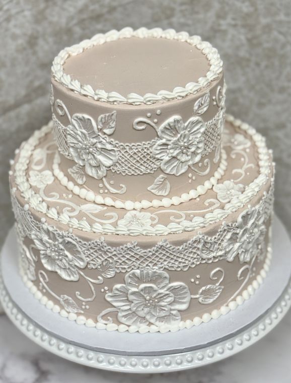 Two-tier blush cake covered in piped white lace and brush-embroidery flowers