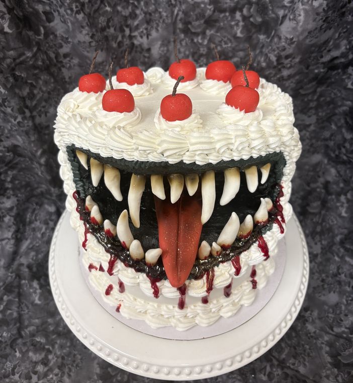 White piped cake with a sculpted monster mouth full of fangs and cherries on top